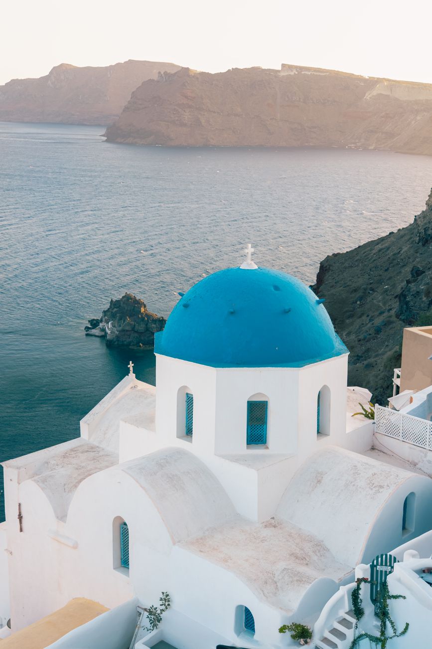 A white Santorini church with a blue dome overlooking the deep blue Aegean sea